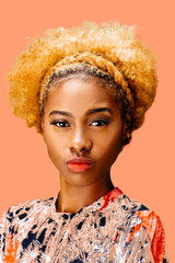 Portrait of a lovely young girl with bleached curly hair looking at camera, isolated on a pink background	