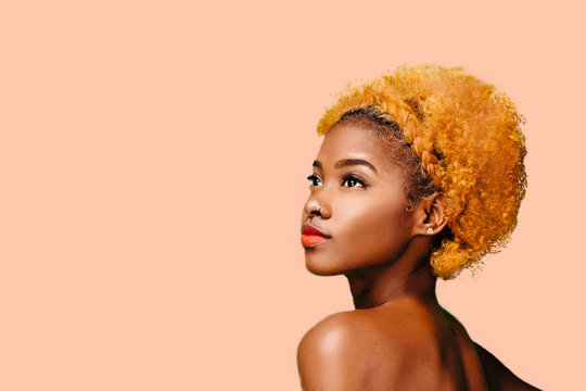 Portrait of a lovely young girl with bleached curly hair looking up, isolated on a peach background	