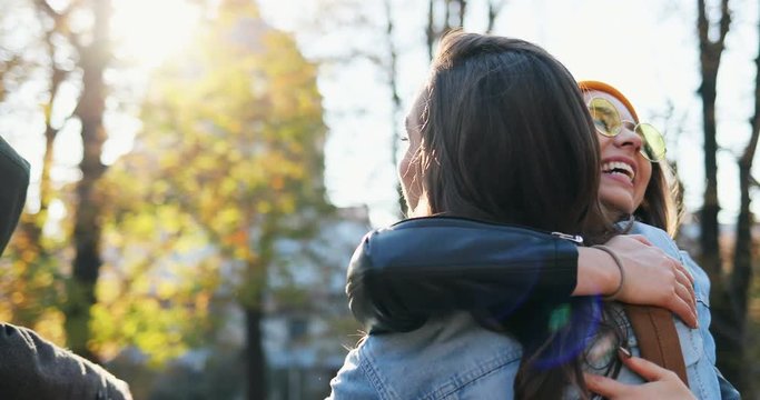 Close up of the young cheerful hipster friends of boys and girls meeting in the park at fall, greeting and hugging. Outdoors.