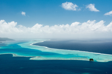 Aerial view on lagoon with blue and turquoise water, barrier reef, blue sky and white clouds of...