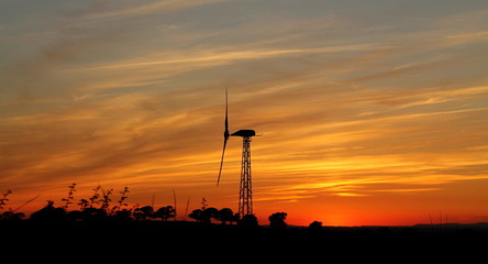 Fototapeta na wymiar A dramatic intense orange sunset with silhouetted wind turbine and horizon.