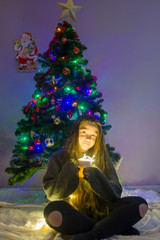 Young girl with christmas tree soft focus low light. Young girl holding sparklers for christmas during winter alone, with beautiful christmass tree bokeh lights in the background