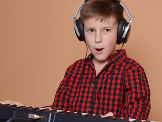 Cute Caucasian boy is emotionally singing and playing the electric piano. He is using headphones...