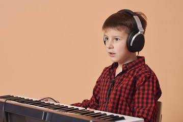 Cute Caucasian boy is  singing and playing the electric piano. He is using headphones while having...