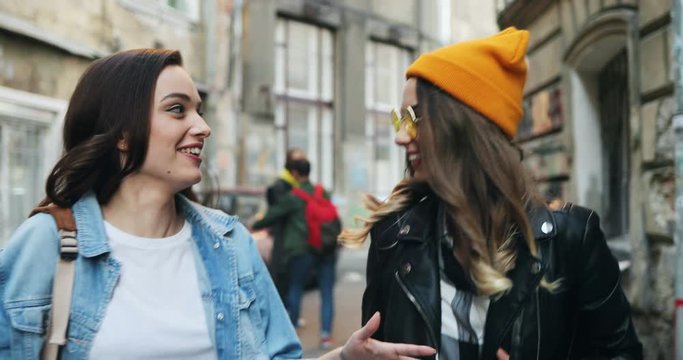 Close up of the two Caucasian young stylish women best friends walking the street in slums and talking cheerfully. Outdoor.