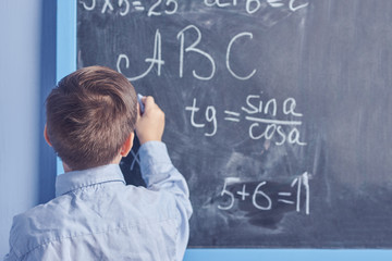 Smart European boy in a blue shirt is standing at the blackboard and solving mathematical problems....
