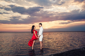Fototapeta premium young couple in love holding hands in the sea against the backdrop of a beautiful sunset.