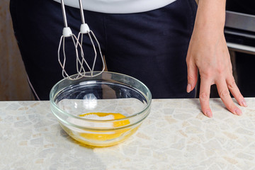 A woman is cooking in her kitchen, about to bake a cake. Beat chicken egg yolks with sugar with a kitchen mixer