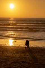 Naklejka premium Silhouette of a couple taking a selfie against the sunset over the Atlantic Ocean