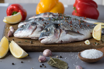 Closeup of two fresh dorado (fish) sprinkled with spices on a wooden board. Semifinished