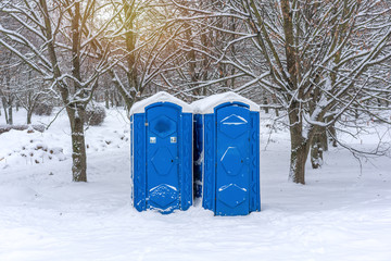 two blue portable plastic toilets in the park in winter