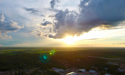 Floating clouds in the sky at sunset, sun glare, look down forests and fields in Finland. Summer aerial view of the drone in the afternoon, the horizon line.
