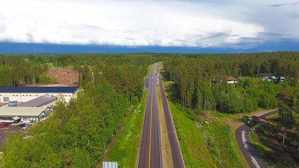 Fototapeta na wymiar Summer aerial photography asphalt road in the countryside through the forest in Finland. Technical buildings and cars top view. The sky in the clouds and the horizon.