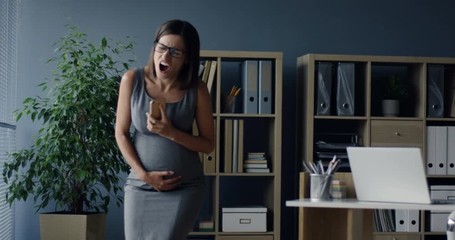 Young beautiful pregnant woman talking on the phone in the office at her working place as feeling strong pain spasm in her belly.