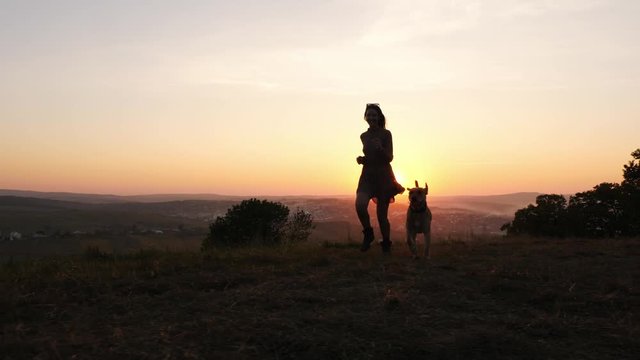 Adorable young woman playing running with her cute dog on nature during sunset