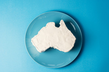 vanilla cream cake in a shape of the Australian continent on blue background. 