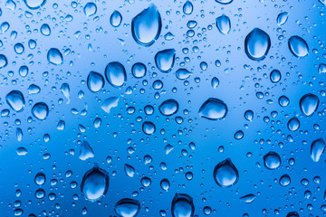 Water drops on glass window blue background after the rain in the autumn fall