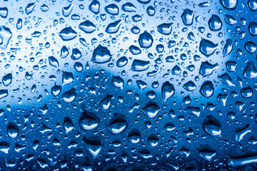 Water drops on glass window blue background after the rain in the autumn fall