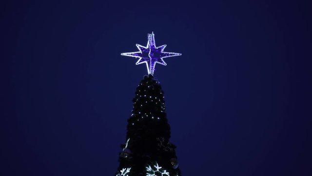 Holiday tree decorated with Christmas glowing decorations outdoor in city street. Real time 4k video footage.