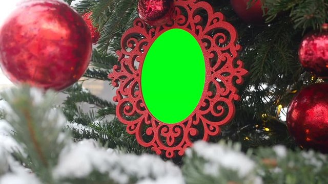 Curly Carved Picture Frame Hanging on Fir Tree Sprinkled With Snow. Inserted Green Chroma Key Into the Red Frame. Empty Photo Frame Christmas and New Year Background, Blank Mockup Template