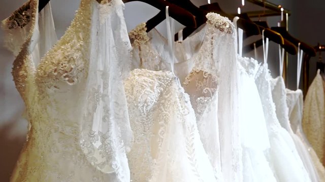 Close-up dolly of wedding dresses on rack. Boutique bridal shop with famous brand exclusive dresses on display. Moving along beautiful gowns in Asian wedding dress shop in China.