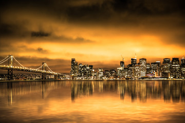 View of San Francisco skyline under golden sunset sky with lights and Bay Bridge