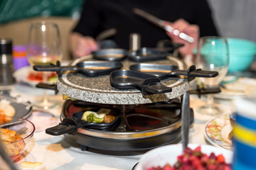 traditional swiss electric raclette stone grill unit with individual skillets on christmas table