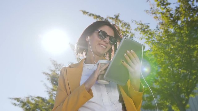 Close up of caucasian busy businesswoman who uses tablet computer while she is standing near office centre during a lunch break. Outdoors