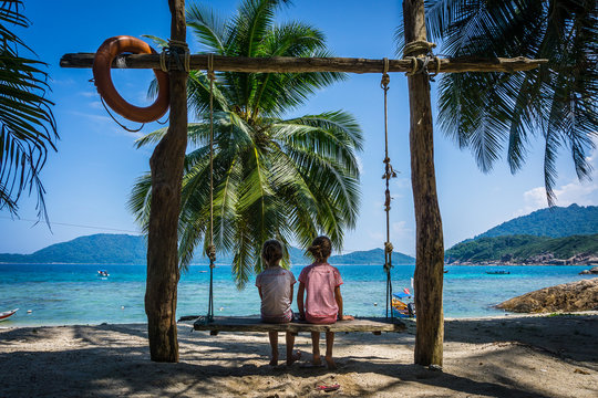 Kids staring at the ocean on a swing at the beach of Perhentian island, a tropical paradise in Malaysia