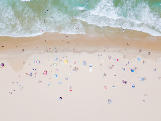 An aerial view of people on the beach with blue water on hot summer's day