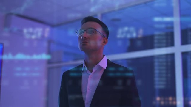 The businessman in glasses working in the dark room on the hologram background