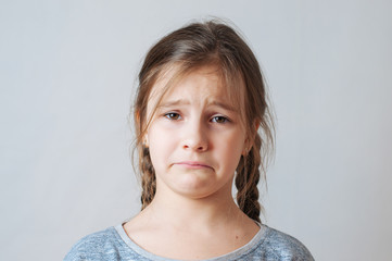 Sad little girl with pigtails portrait on a neutral background