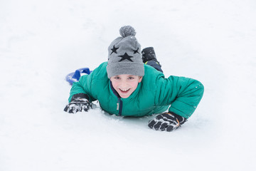 Fototapeta na wymiar Boy lying in the snow on his belly and smiles. Portrait close-up