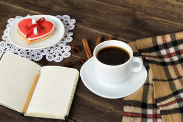 Cup of coffee, heart shaped cookies with message, notebook, pencil and checkered plaid on a brown wooden table. Holiday planning