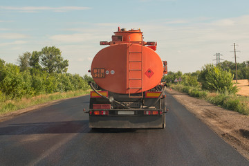 Orange tank truck rides on a country road against a blue sky. Back view