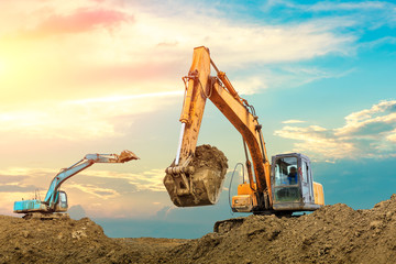 Two excavators work on construction site at sunset