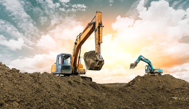 Two excavators work on construction site at sunset