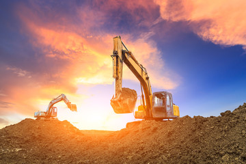 Two excavators work on construction site at sunset