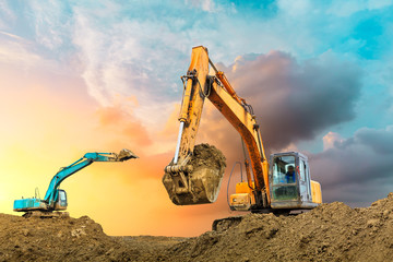 Two excavators work on construction site at sunset
