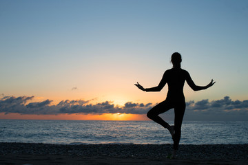 Fototapeta na wymiar silhouette of person doing yoga on the beach at sunrise