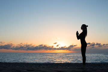 silhouette of woman doing greeting to the sun on the beach at sunrise, morning yoga