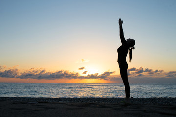 Human silhouette doing yoga on the beach at the dawn