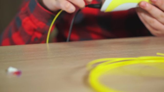Teen boy inserts a piece of yellow ABS plastic in a 3D pen. He creates a plastic 3D figure.