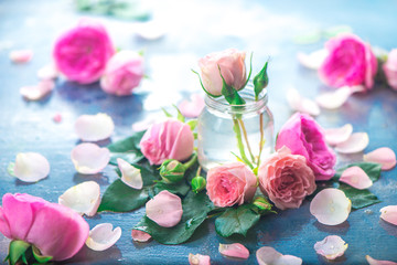 Glass bottles with pink peony roses on a light background with copy space. Feminine header with petals and flowers in pastel tones