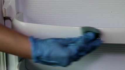 female hand in blue rubber glove slowly washes the refrigerator door close-up