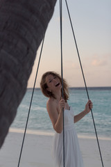 Beautiful happy woman on a swing attached to a palm during honeymoon. Sunset in the Maldives