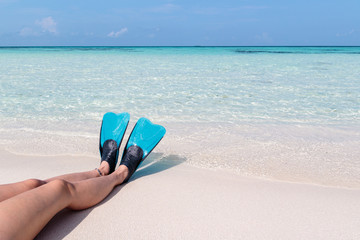 woman legs with flippers on a white beach in the Maldives. Crystal clear blue water as background