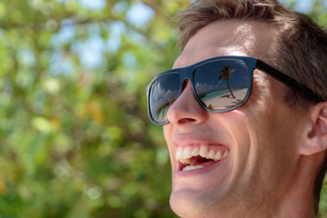 palm tree, white beach and crystal clear blue water reflected in the sunglasses of a happy man. Maldives