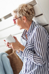 Obraz premium Mature good looking woman sitting in the room with mug on her hand and smile