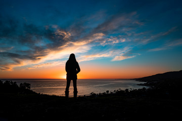 Fototapeta premium Woman silhouette stares at sunset and ocean
